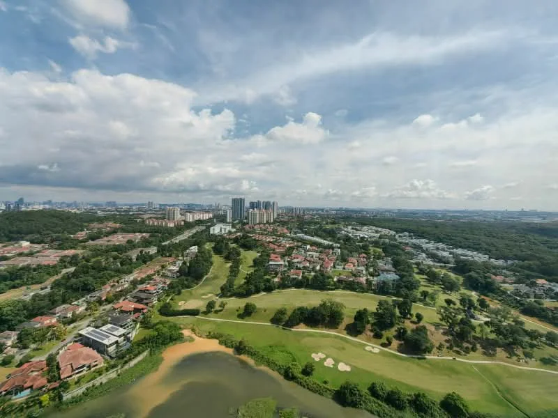 Exterior type: high-rise condominium; features: city skyline view, lush greenery, golf course, water body, urban residential area, surrounded by low-rise houses, open sky, cloudy weather; style: modern.