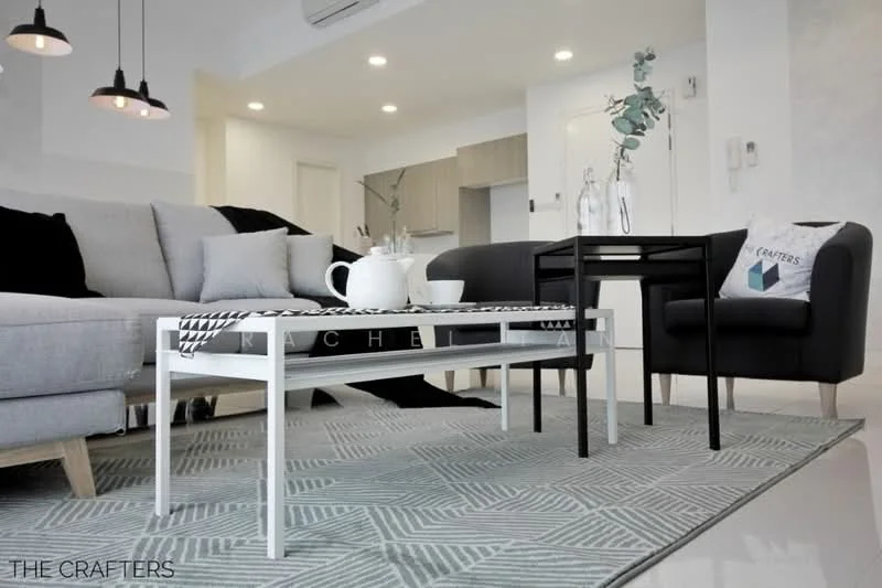 Living features: grey fabric sofa, black leather armchair, white coffee table, area rug with geometric pattern, pendant lighting, decorative vase with plant, wall-mounted air conditioning unit, neutral painted walls, light-colored flooring, throw pillows with patterns; style: modern.