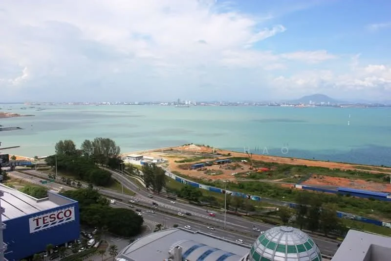 Exterior features: view of the sea, urban skyline in the distance, surrounded by greenery, near a major road, visible commercial building (Tesco), open water, construction site in the foreground; style: modern.