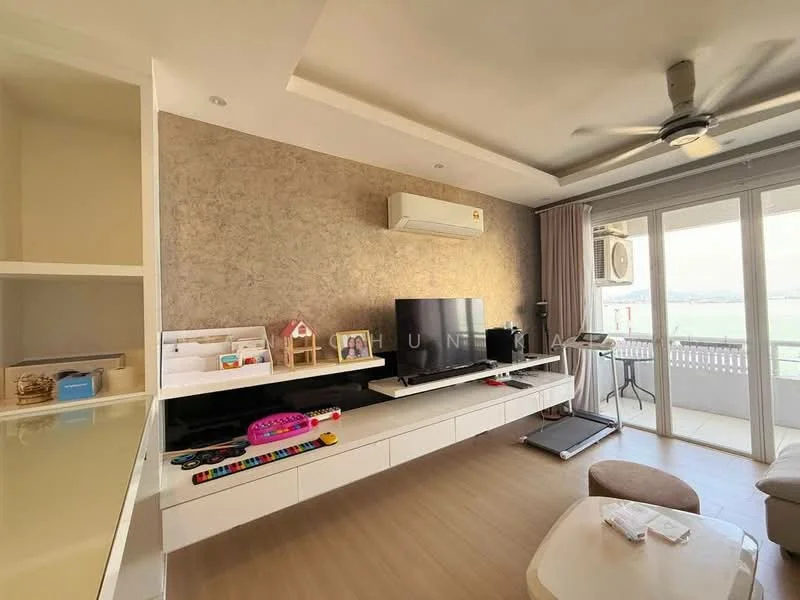 Living features: light wood flooring, feature wall with textured finish, white wall-mounted TV unit, large flat-screen TV, 5-blade ceiling fan, sliding glass door, floor-to-ceiling windows, air conditioning unit, decorative items on shelves, children's toys, coffee table, area rug; style: modern; view: sea.