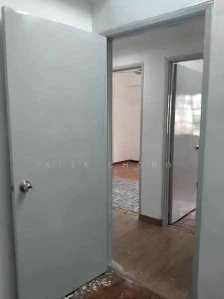 Room features: white painted walls, wood flooring, grey door, door frame, light switch, visible doorways, neutral color scheme, natural light from adjacent room.