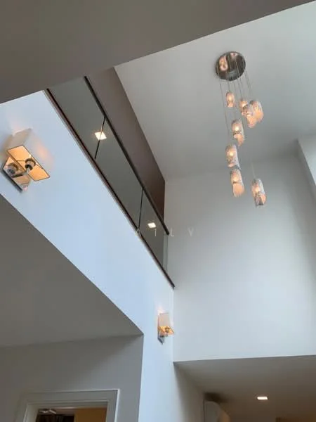 Room features: white painted walls, high ceiling, glass railing, chandelier with multiple glass pendants, wall sconces with fabric shades, recessed downlights; style: modern.