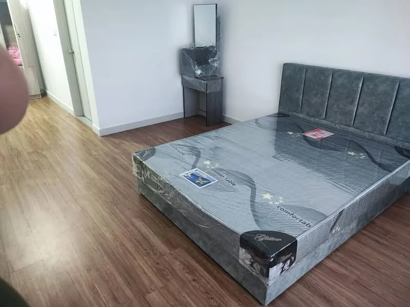 Bedroom features: queen-size bed with grey upholstered headboard, wooden flooring, white painted walls, mirror on a small vanity table, decorative items on bed, natural light from window, minimalist decor; style: modern.