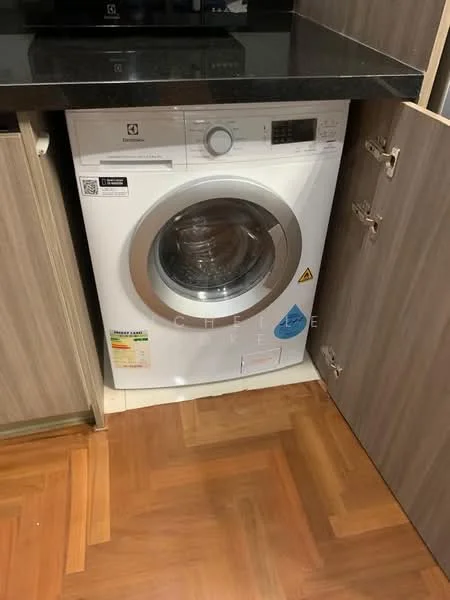 Laundry features: front-load washing machine in white, black countertop, wood cabinetry in light brown, parquet wood flooring, space-saving design with cabinet doors; style: modern.