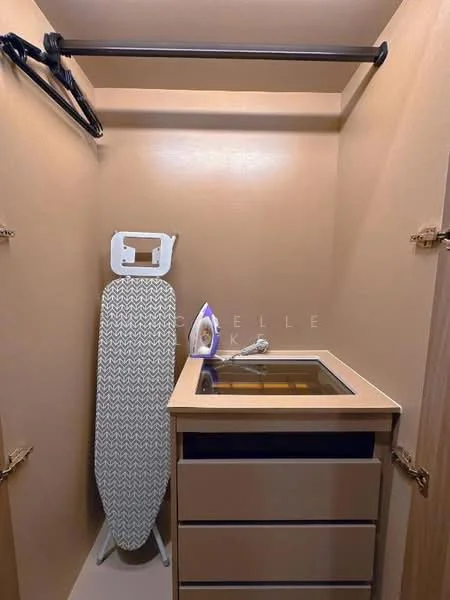 Room features: ironing board, iron, built-in cabinet, drawer unit, neutral painted walls, shelf above, clothes hanging rod.