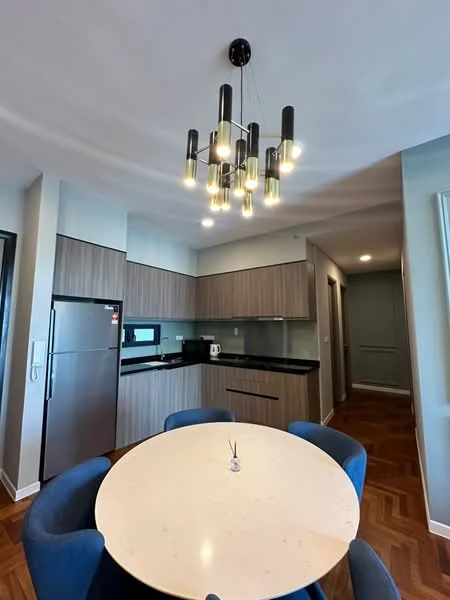 Kitchen features: black granite countertop, wood cabinetry in light brown, stainless-steel fridge, built-in microwave, kettle, pendant light fixture with multiple bulbs, black backsplash, 4-seater round dining table, blue upholstered dining chairs, wood flooring with herringbone pattern, recessed lighting, open layout; style: modern.
