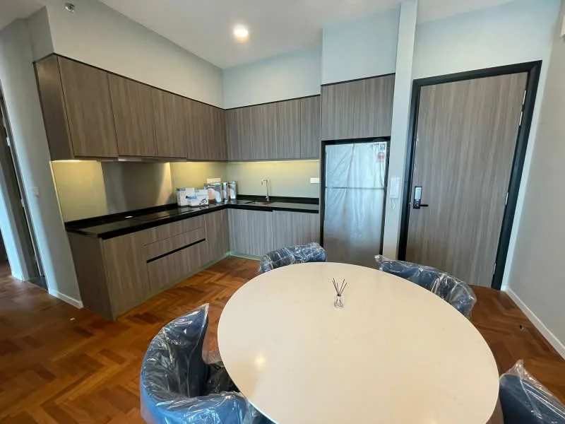 Kitchen features: wood cabinetry in light brown, black granite countertop, stainless-steel fridge, single-bowl stainless-steel sink, chrome pull-down faucet, built-in oven, 4-burner gas hob, tile backsplash, recessed downlights, wood flooring in herringbone pattern, open layout to dining area, kitchen island, dining table with round white top, upholstered dining chairs in blue; style: modern.