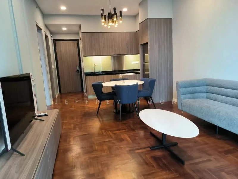 Living features: parquet wood flooring, light blue painted walls, ceiling light fixture with multiple bulbs, sofa in light grey fabric, round white coffee table, TV console in light wood, wall-mounted TV, dining table with white top and four blue upholstered chairs, kitchen area visible in background with dark cabinetry, open-plan layout; style: modern.
