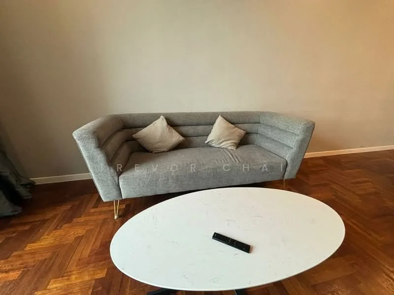 Living features: 3-seater fabric sofa in grey, 2 decorative cushions, round coffee table with white top, black remote control on table, parquet wood flooring, plain painted walls in neutral color, curtains in grey fabric; style: modern.