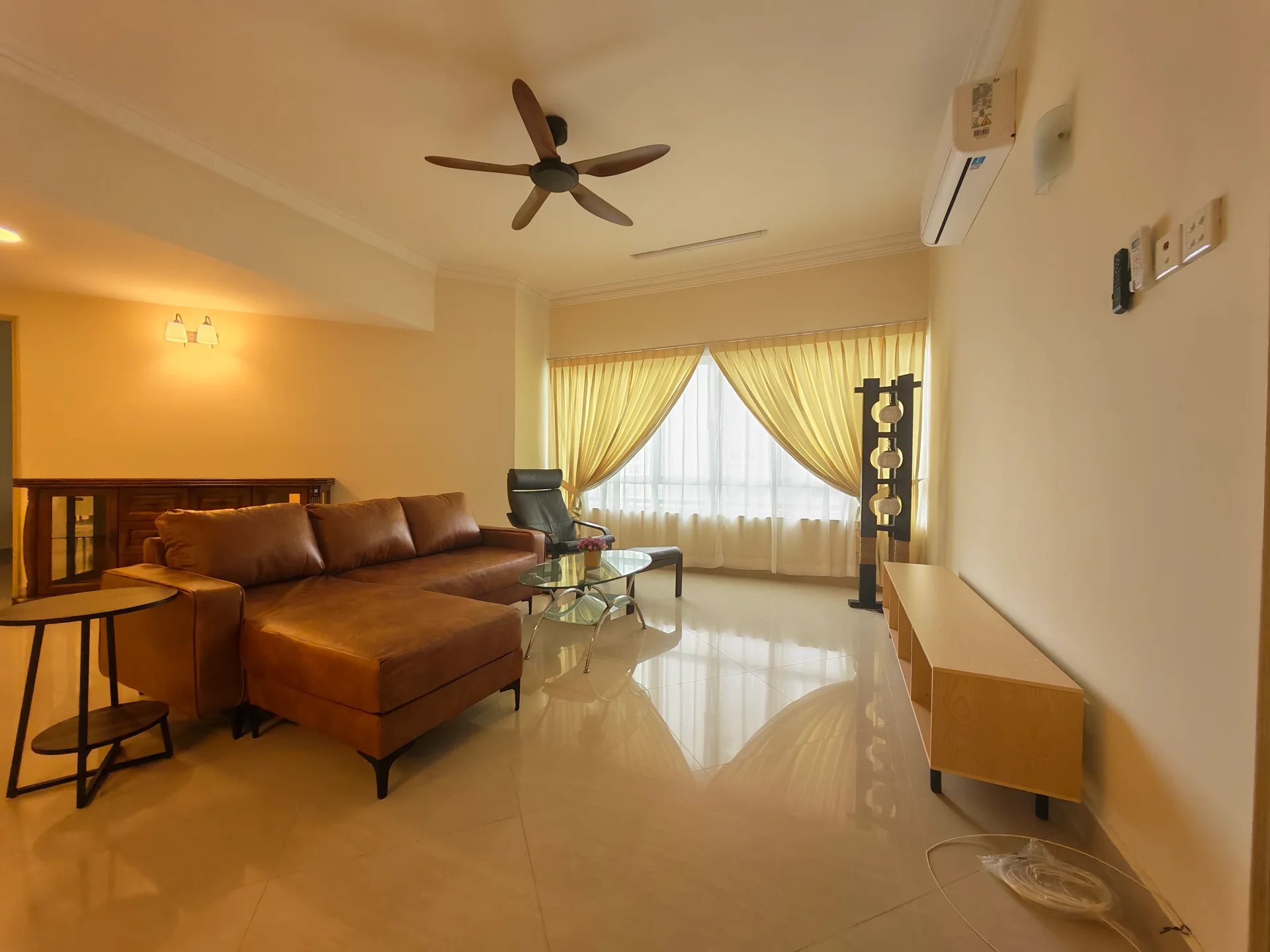 Living features: 5-blade ceiling fan with light, sofa in brown leather, glass coffee table, side table with black metal frame, TV console in light wood, floor-to-ceiling windows, sheer curtains in yellow, marble flooring, wall-mounted air conditioning unit, decorative floor lamp; style: modern.