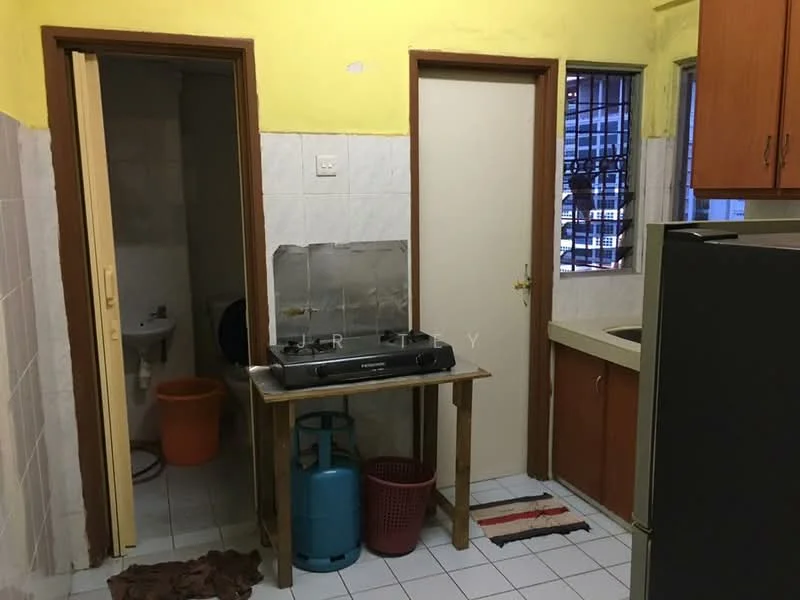 Kitchen features: yellow painted walls, white tiled flooring, wooden cabinetry, stainless-steel gas stove, sink, refrigerator, table, window with security bars, door leading to bathroom, door leading to hallway. Bathroom features: white tiled walls, white tiled flooring, toilet, orange waste bin.