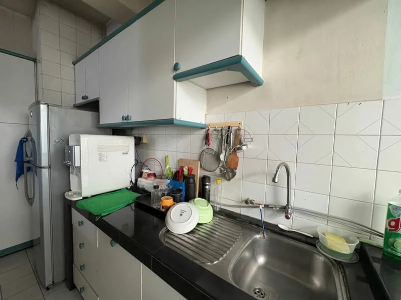 Kitchen features: white cabinetry with blue trim, black countertop, single-bowl stainless-steel sink, chrome faucet, wall-mounted dish rack, white tiled backsplash, ceramic tile flooring, refrigerator, microwave, various kitchen utensils, green dish drying mat, stacked plates and cups; style: functional.