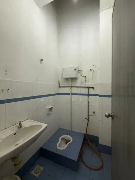 Bathroom features: squat toilet, wall-mounted sink, blue tiled flooring, white tiled walls, shower area with no enclosure, exposed plumbing, single mirror, no visible storage, basic lighting, minimal decor.