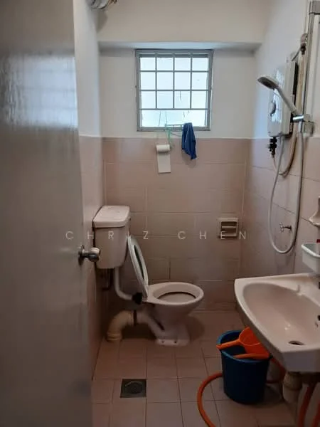 Bathroom features: white tiled walls, pink tiled walls, ceramic tile flooring, one-piece toilet, sink with pedestal, mirror above sink, shower head, window with grid, cleaning bucket, shower hose, towel rack.