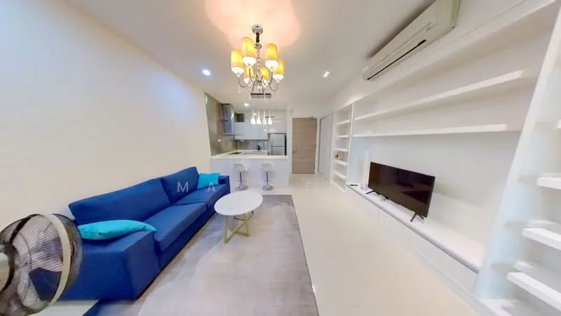 Living features: blue fabric sofa, white coffee table, wall-mounted TV, built-in shelving unit, chandelier with multiple bulbs, recessed lighting, air conditioning unit, light-colored walls, neutral tile flooring, decorative area rug; style: modern. Kitchen features: open kitchen layout, bar stools, kitchen cabinetry, countertop, refrigerator, stainless-steel appliances; style: modern.