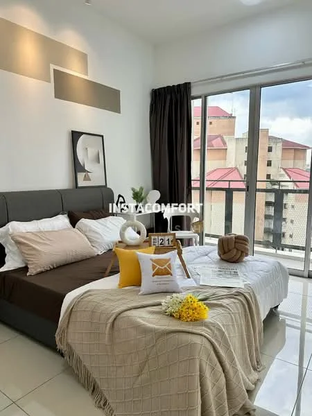 Bedroom features: king-size bed with grey upholstered headboard, white bedding with decorative pillows, cream throw blanket, floor-to-ceiling windows, blackout curtains, white walls, tile flooring, decorative artwork on wall, small indoor plant, side table with lamp, decorative basket, yellow accent pillows; style: modern; view: city.