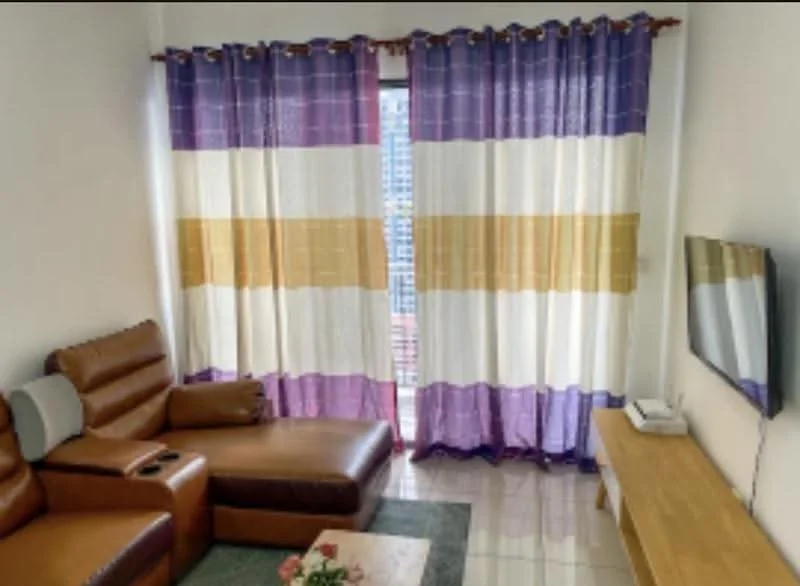 Living features: brown leather sectional sofa, recliner chair, flat-screen TV on wooden console, white walls, glossy tile flooring, large window with sheer curtains, decorative area rug, coffee table with floral arrangement; style: modern.