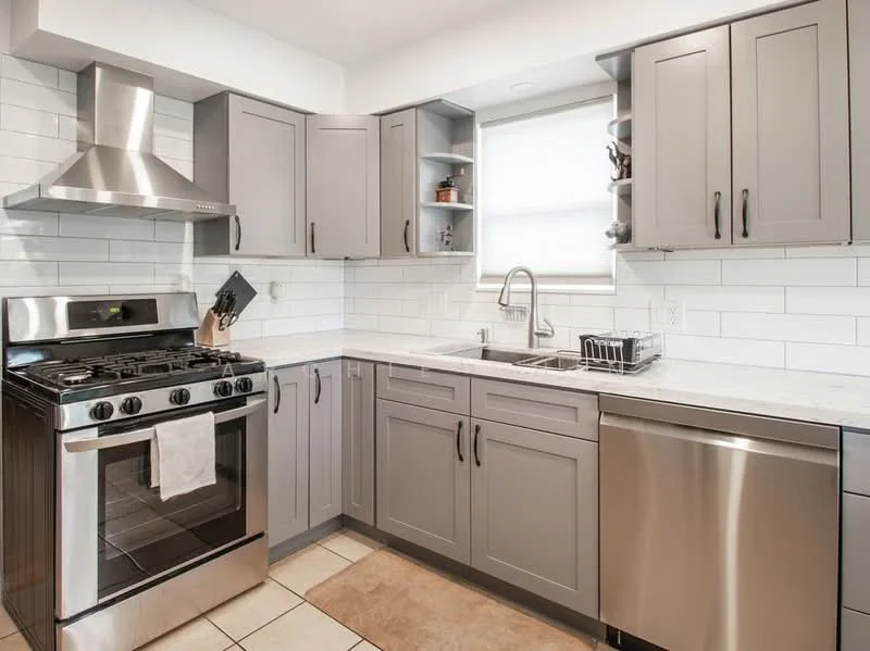 Kitchen features: stainless-steel gas range oven, stainless-steel dishwasher, stainless-steel sink, chrome pull-down faucet, grey shaker cabinets, white subway tile backsplash, marble countertop, tile flooring, window with natural light, open shelving, kitchen utensils on counter, dish rack; style: modern.