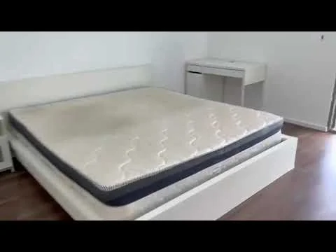 Bedroom features: queen-size bed, mattress on bed frame, wooden flooring, white painted walls, study desk, window with natural light, built-in wardrobe, minimalist decor; style: modern.