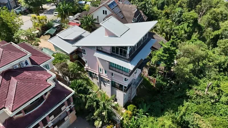 Exterior type: detached bungalow; features: pink painted facade, metal roofing, multiple pitched roofs, large windows, surrounded by greenery, balconies on upper levels, landscaped garden, driveway with interlocking pavers; style: modern.