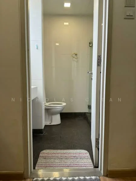 Bathroom features: white tiled walls, grey floor tiles, one-piece toilet, single-sink vanity with white cabinet, mirror above vanity, shower fixture on wall, recessed ceiling lights, door with handle, bath mat on floor; style: modern.