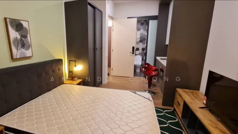 Bedroom features: queen-size bed, upholstered headboard, wooden bedside table, wall-mounted TV, flooring in wood, green area rug, decorative wall art, recessed lighting, sliding wardrobe doors, open doorway to bathroom, wall with dark paint, light green accent wall; style: modern. Room features: open doorway, kitchenette area, bar stools, light-colored cabinetry, neutral wall color.