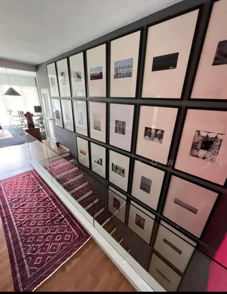Room features: wood flooring, grey accent wall, gallery wall with framed photographs, glass railing, area rug with geometric pattern, recessed lighting, open space, natural light from windows; style: modern.