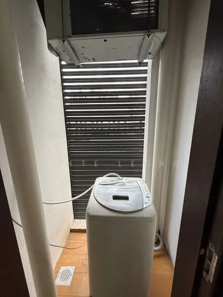 Laundry features: top-load washing machine, ventilation window, slatted window coverings, drainage grate on floor, wooden flooring, white walls.