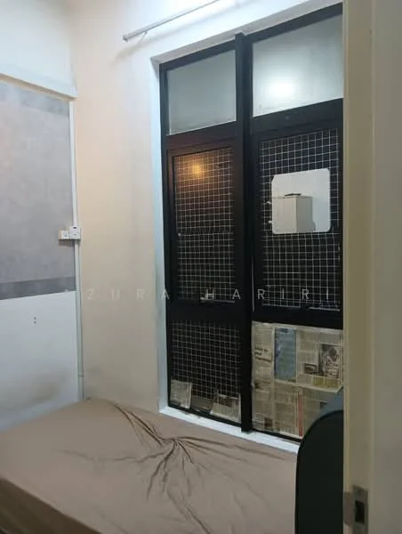 Bedroom features: single bed, plain beige bedspread, white painted walls, grey accent wall, floor-to-ceiling windows, metal grille window, newspaper clippings on window sill, light fixture on ceiling.