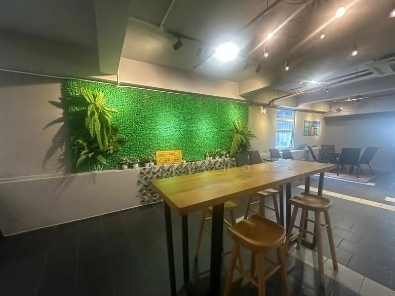 Room features: green wall with artificial plants, wooden dining table, 3 wooden bar stools, grey painted walls, black tile flooring, hanging pendant lights, decorative wall with stone cladding, seating area with chairs in the background; style: modern.