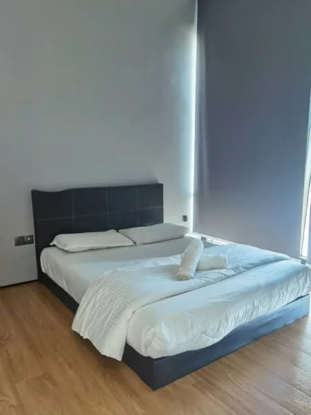 Bedroom features: queen-size bed, upholstered headboard, white bedding, wooden flooring, floor-to-ceiling windows, grey curtains, two rolled towels on bed, minimalist decor; style: modern.