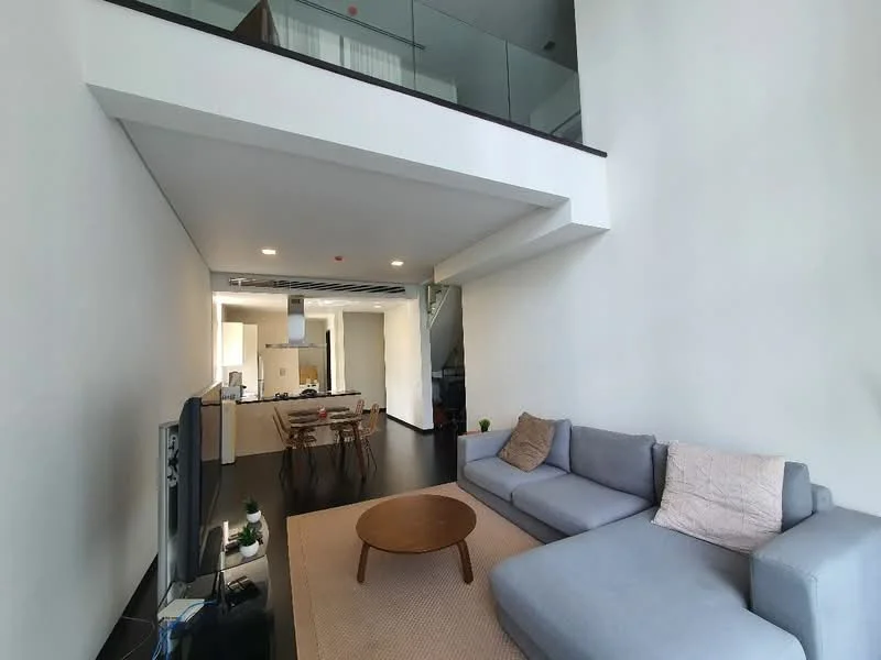 Living features: grey fabric sectional sofa, round wooden coffee table, area rug, wall-mounted TV, recessed downlights, white painted walls, dark wood flooring, open-plan layout to kitchen, glass railing on upper level; style: modern. Kitchen features: kitchen island, stainless-steel appliances, white cabinetry, open shelving, light-colored countertops; style: modern.