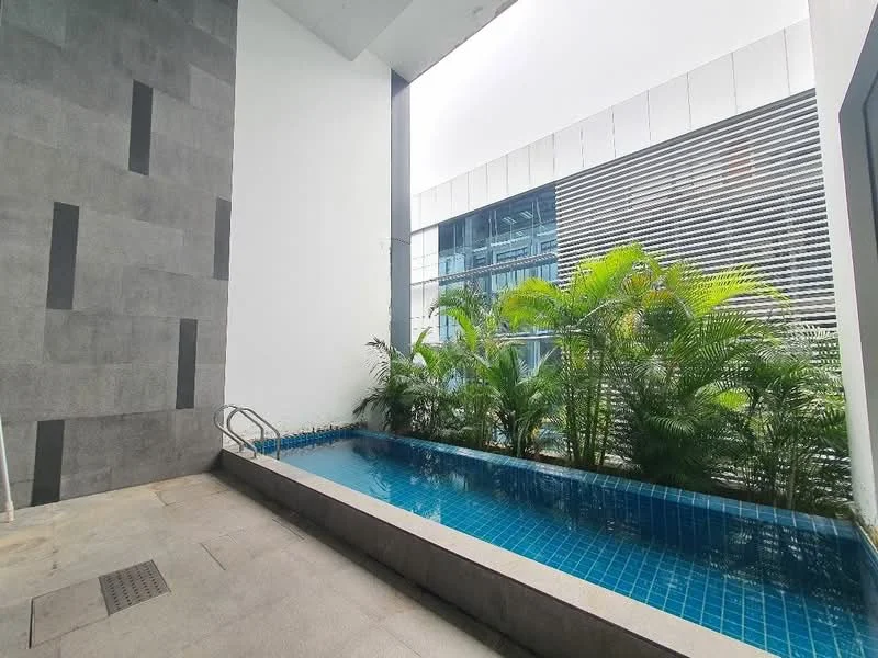 Exterior type: swimming pool deck; features: infinity pool, blue mosaic tile pool, surrounded by tropical plants, grey stone wall, concrete flooring, glass facade of adjacent building, modern architectural design; style: modern.