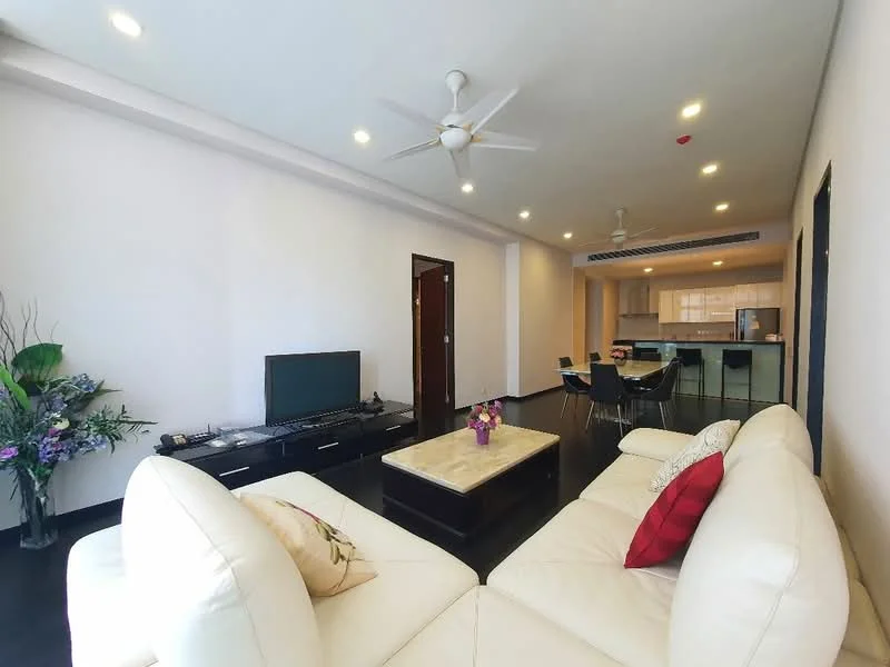 Living features: white painted walls, dark wood flooring, 5-blade ceiling fan with light, sofa in white leather, red accent cushion, coffee table with marble top, TV console, wall-mounted TV, decorative plant, dining area with black dining chairs, open kitchen view, recessed lighting; style: modern.