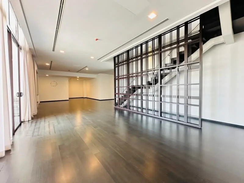 Living features: dark hardwood flooring, white painted walls, large floor-to-ceiling windows, curtains, open space layout, staircase with metal railing, recessed ceiling lights, wall clock, neutral color scheme, no visible furniture; style: modern.