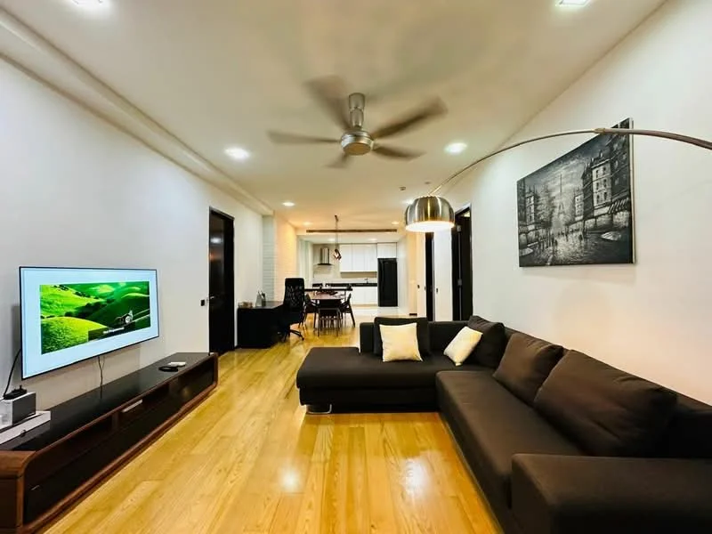 Living features: L-shape sectional sofa in dark grey, 2 white throw pillows, wooden flooring, wall-mounted TV, TV console with storage, 5-blade ceiling fan with light, recessed LED downlights, decorative wall art, open layout to dining area, large windows with natural light; style: modern.