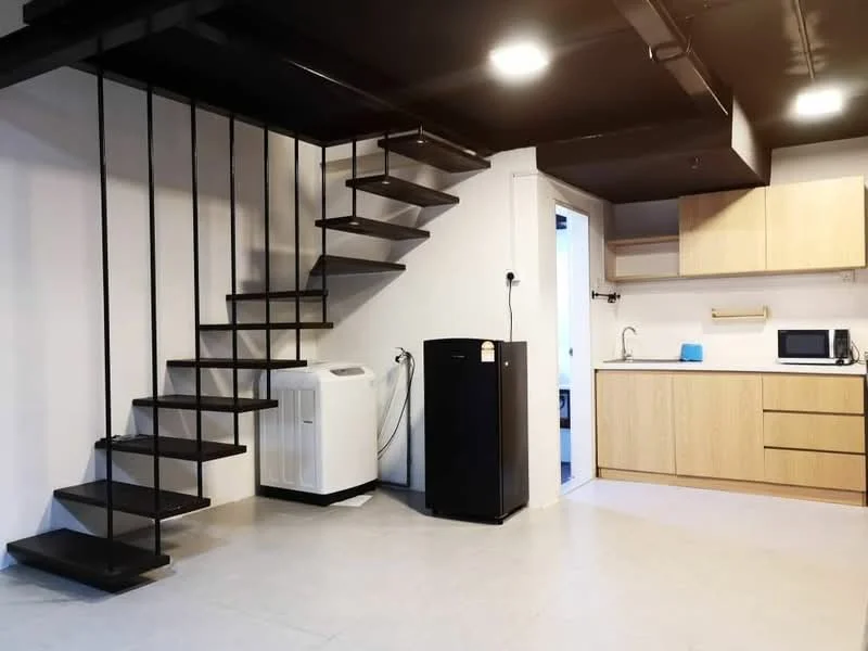 Room features: spiral staircase with metal steps, white wall, black ceiling, light grey flooring, black refrigerator, white washing machine, wood cabinetry in light wood finish, kitchen countertop, microwave, sink, kitchen faucet; style: modern.