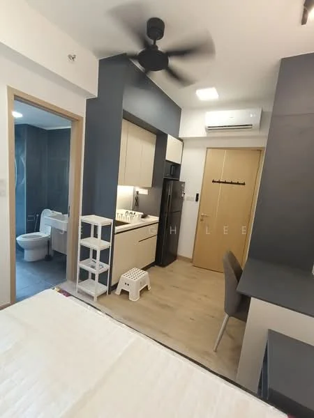 Room features: light wood flooring, white walls, grey accent wall, 5-blade ceiling fan, wall-mounted split AC, kitchenette with cabinets, black refrigerator, stainless-steel sink, chrome pull-down faucet, countertop with storage, study desk with chair, white shelving unit, white step stool, bathroom door, toilet visible in bathroom; style: modern.