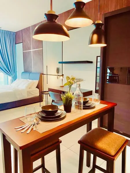 Dining features: wooden dining table, two wooden dining chairs, black dinner plates, glass water bottles, cutlery set, table runner, pendant lighting, decorative plant, white walls, grey curtains, bed visible in background, wood paneling on walls; style: modern.