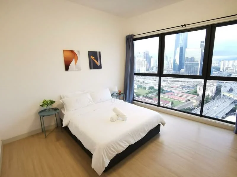 Bedroom features: king-size bed with white bedding, two white towels on the bed, floor-to-ceiling windows, city skyline view, light wood flooring, blue curtains, two framed artworks on the wall, small round side table, green plant on side table; style: modern; view: city.