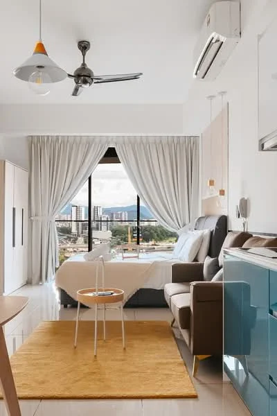 Bedroom features: queen-size bed with upholstered headboard, floor-to-ceiling windows, white sheer curtains, grey accent wall, recessed downlights, 5-blade ceiling fan with light, wooden flooring, decorative mirror, area rug in mustard yellow, armchair in brown leather, small round side table, built-in wardrobe, air conditioning unit; style: modern; view: city.