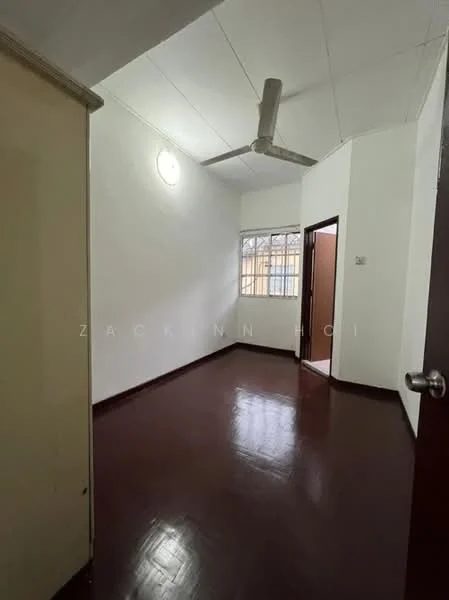 Room features: white painted walls, brown wooden flooring, ceiling fan, window with grid, doorway to adjacent room, light fixture on ceiling, corner wall with no visible decor.