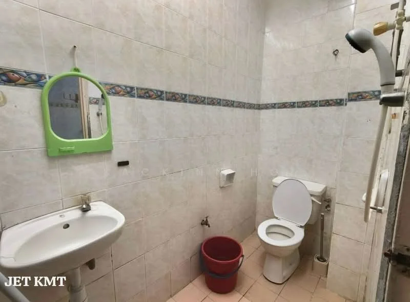 Bathroom features: white tiled walls, pink tiled flooring, single-sink vanity with mirror, white toilet, shower with wall-mounted faucet, green framed mirror, decorative border tile, red bucket.