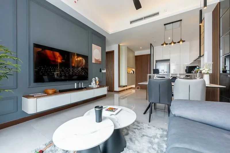 Living features: grey accent wall, white painted walls, marble coffee table, black base coffee table, 3-seater fabric sofa in grey, wall-mounted TV, TV console with storage, area rug with geometric pattern, recessed downlights, ceiling fan, decorative plant, framed artwork, open layout to kitchen, sliding door to balcony; style: modern. Kitchen features: kitchen island, stainless-steel appliances, white cabinetry, black countertop, pendant lighting, open shelving, recessed downlights; style: modern.