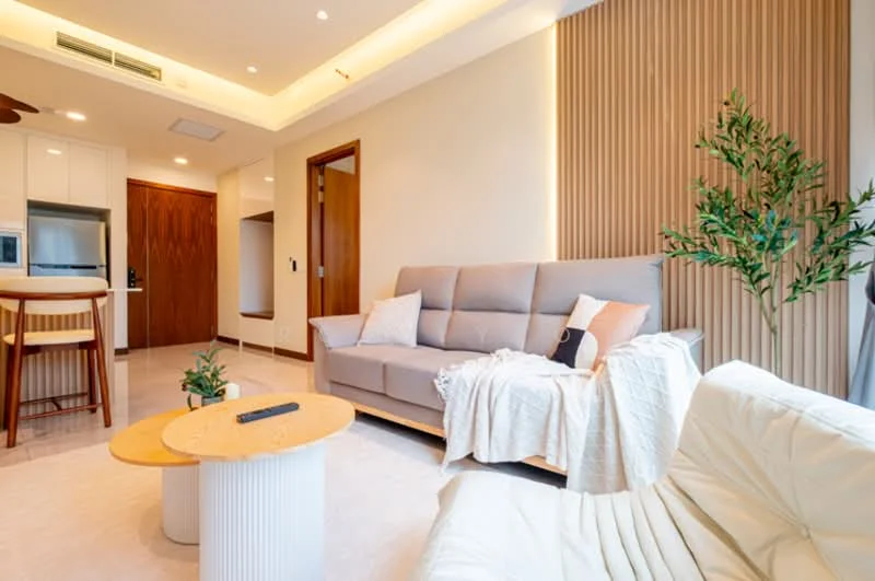 Living features: 3-seater fabric sofa in light grey, 2-seater fabric sofa in white, round coffee table with marble top, wooden dining chairs, wooden dining table, decorative houseplant, wall-mounted TV, recessed LED downlights, wood panel accent wall, cream painted walls, light-colored tile flooring, ceiling with cove lighting; style: modern.