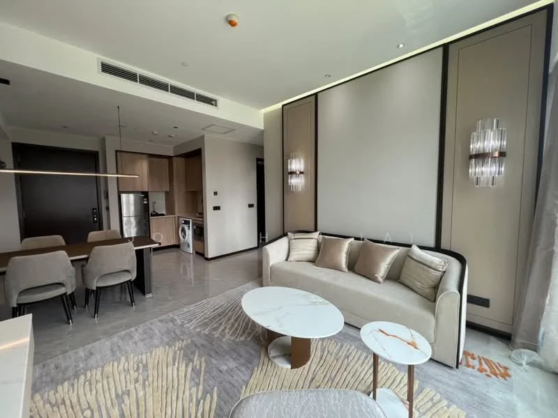 Living features: sofa in light beige fabric, coffee table with marble top, area rug with geometric pattern, wall-mounted TV, dining table for 4 with upholstered chairs, recessed downlights, floor-to-ceiling windows, grey accent wall, built-in cabinetry, washer-dryer combo, stainless-steel fridge, open-plan layout with kitchen visible; style: modern.