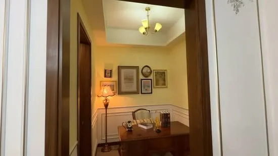 Study features: yellow painted walls, wood paneling, wooden flooring, tray ceiling, 3-bulb ceiling light, table lamp, wooden desk, framed artwork, decorative wall clock, books on desk; style: traditional.
