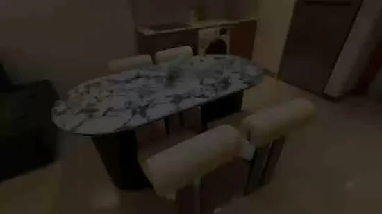 Dining features: oval marble dining table, 4 upholstered dining chairs, cream-colored upholstery, polished tile flooring, kitchenette in background, washing machine visible, refrigerator visible, neutral wall color; style: modern.