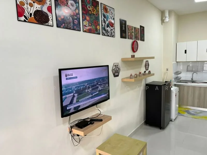 Living features: wall-mounted TV, wooden TV console, decorative wall art with floral patterns, light-colored walls, grey tiled flooring, refrigerator, kitchen area visible in background, open shelving, small wooden table, decorative items on shelves; style: modern.