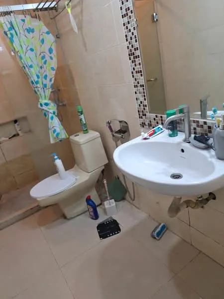 Bathroom features: white ceramic toilet, single-sink vanity with white countertop, chrome basin mixer faucet, shower area with glass partition, tiled walls with mosaic accents, light beige floor tiles, shower curtain with floral pattern, toiletries on sink and floor, mirror above sink; style: modern.